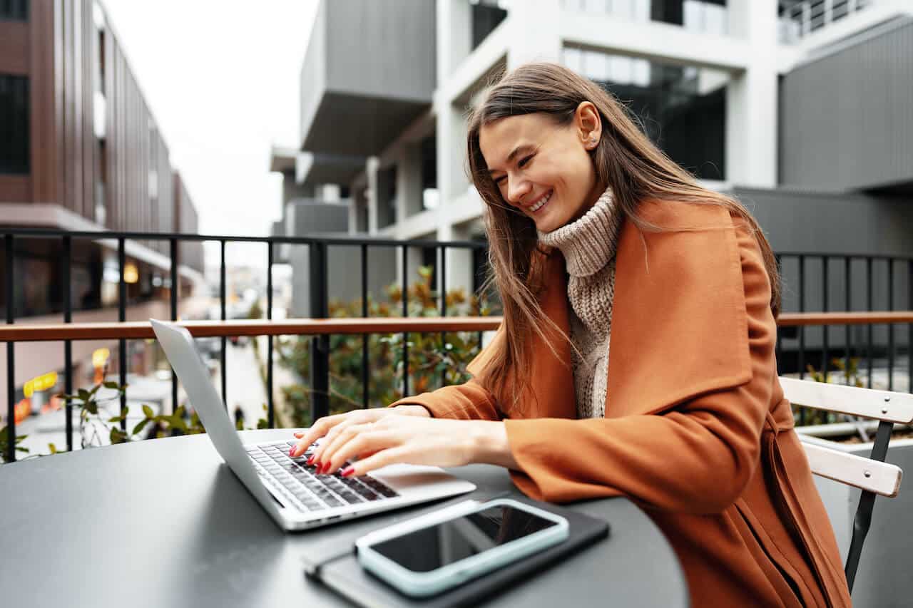 Eine Frau sitzt mit dem Laptop und dem Smartphone im Freien beim Arbeiten